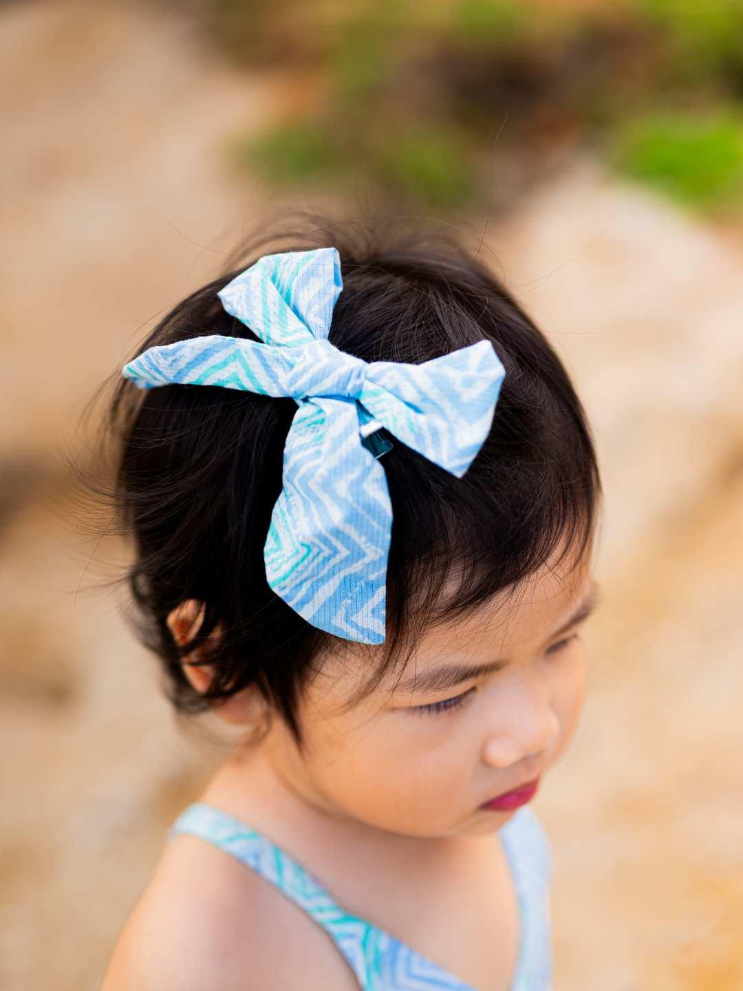 Child wearing an azure cotton headband with white wave pattern, styled in a large bow, sustainable material.