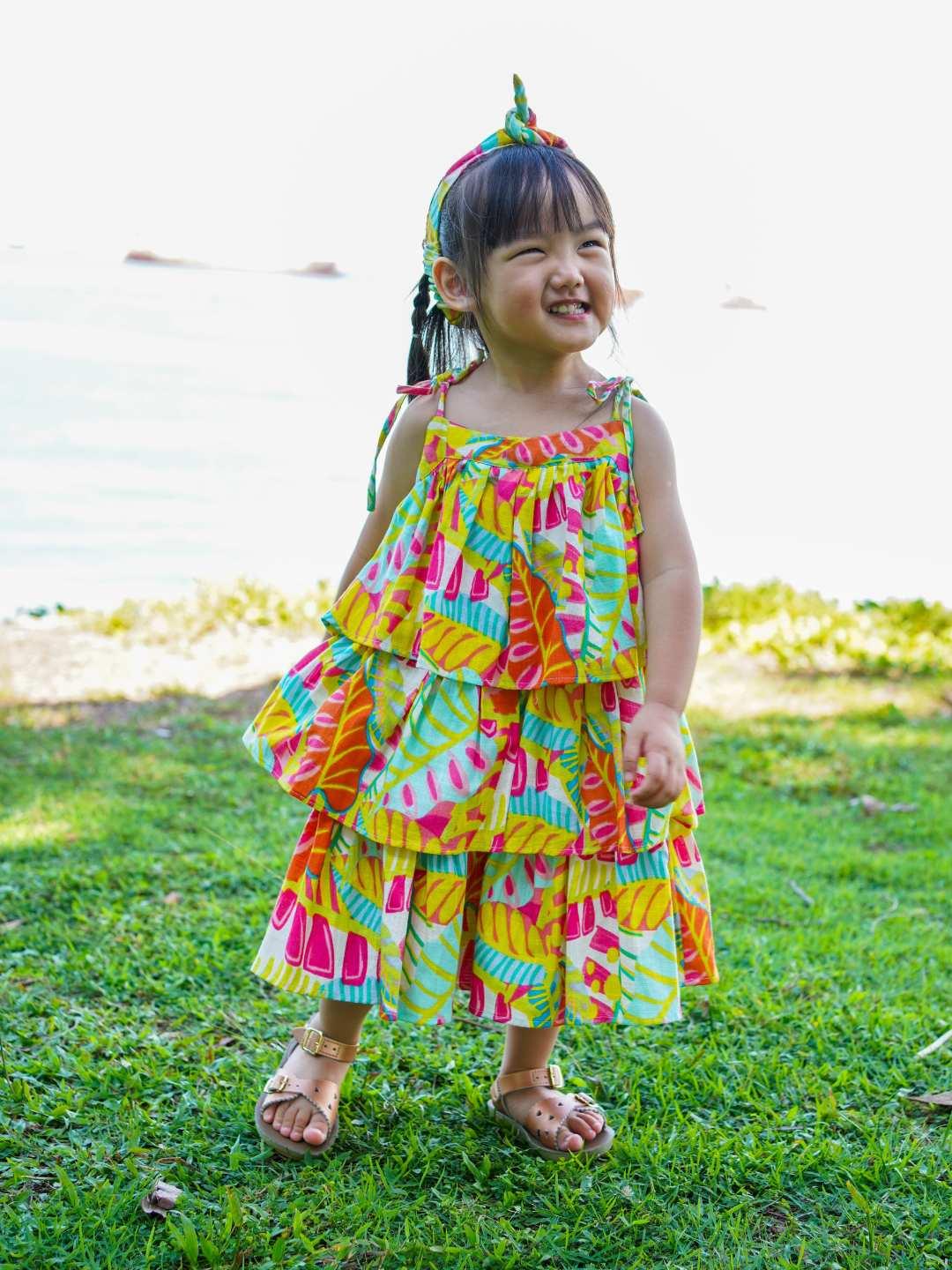 Girls tiered cotton dress in vibrant sunset bloom floral print, sleeveless with ruffled layers, sustainable and casual style .