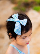 Child wearing an azure cotton headband with white wave pattern, styled in a large bow, sustainable material.