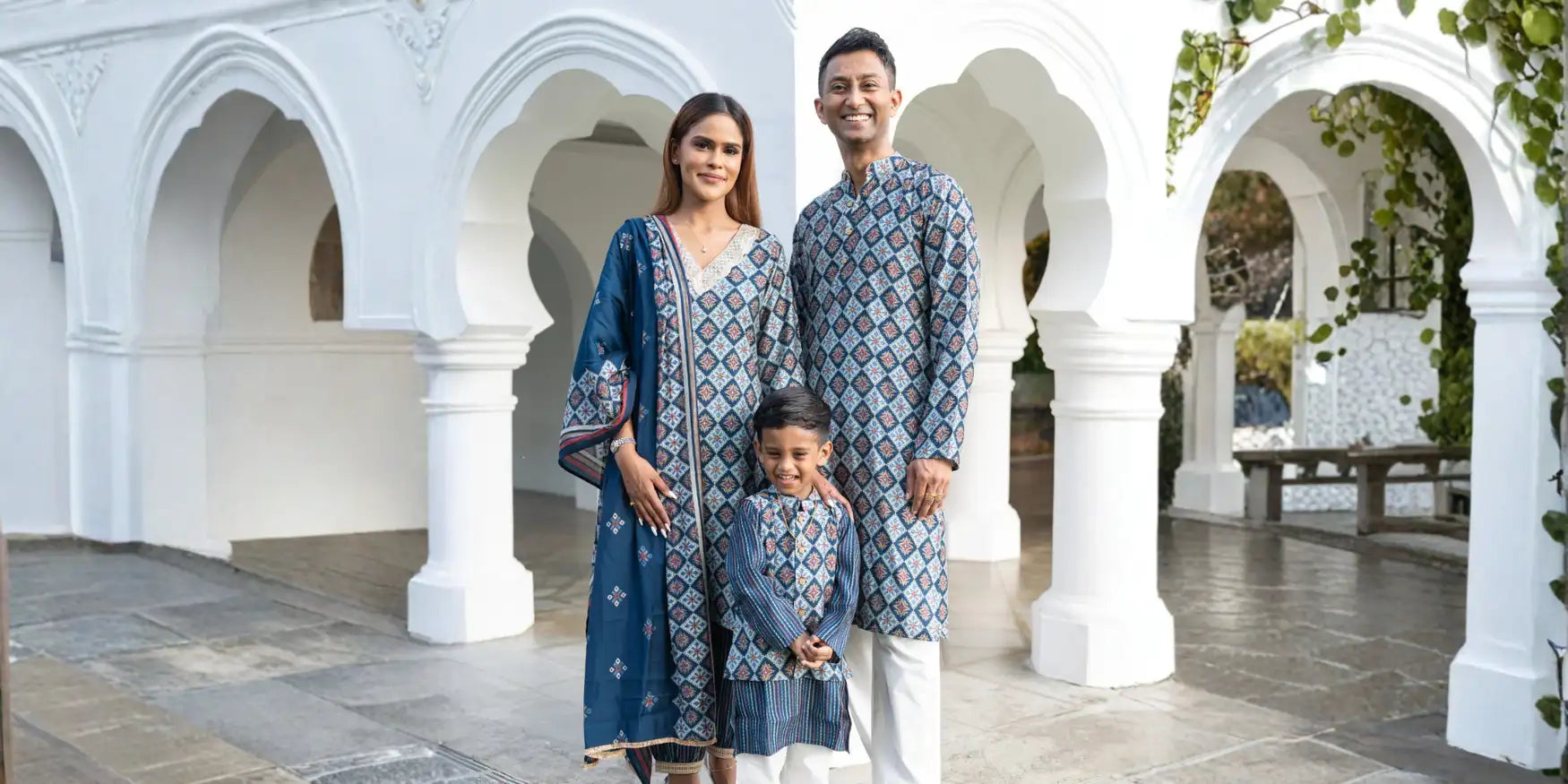 Family of three wearing coordinated blue printed ethnic outfits in a heritage courtyard